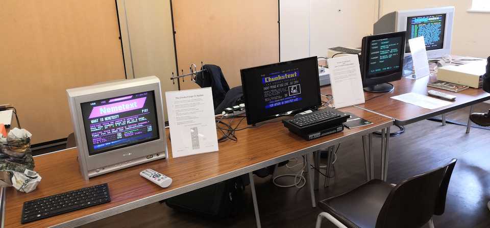 An assortment of TVs on tables, displaying teletext, alongside an assortment of vintage computer hardware.